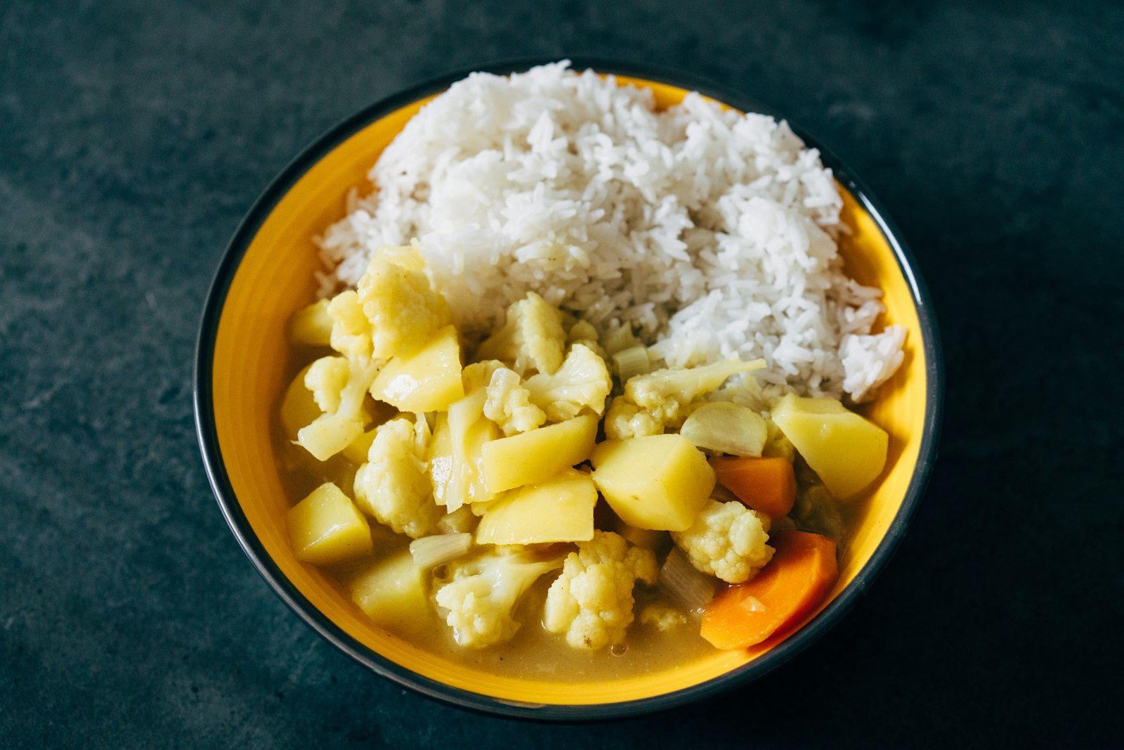 A yellow bowl of potato and cauliflower curry served with white rice